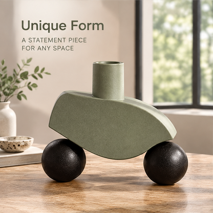Empty sculptural vase showing a curved sage-green body, cylindrical neck and black spherical forms